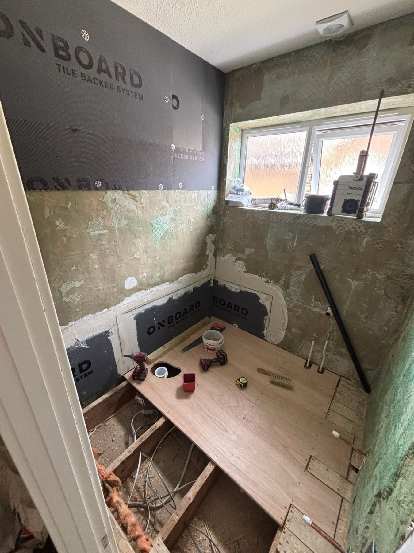 The same bathroom mid-installation with tile backer boards and first-fix plumbing