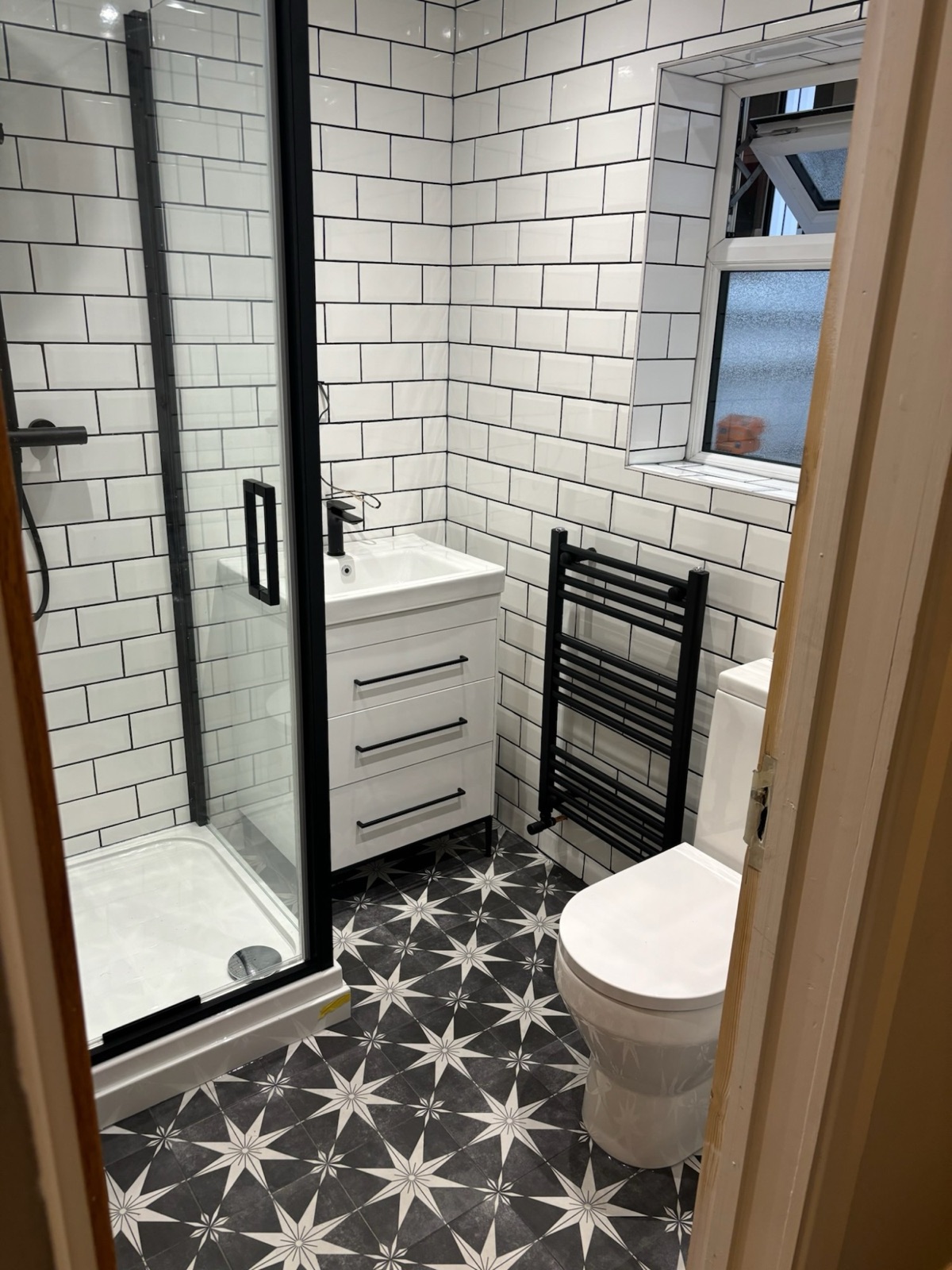 Modern monochrome shower room with white metro tiles, black-framed shower screen and star-pattern floor