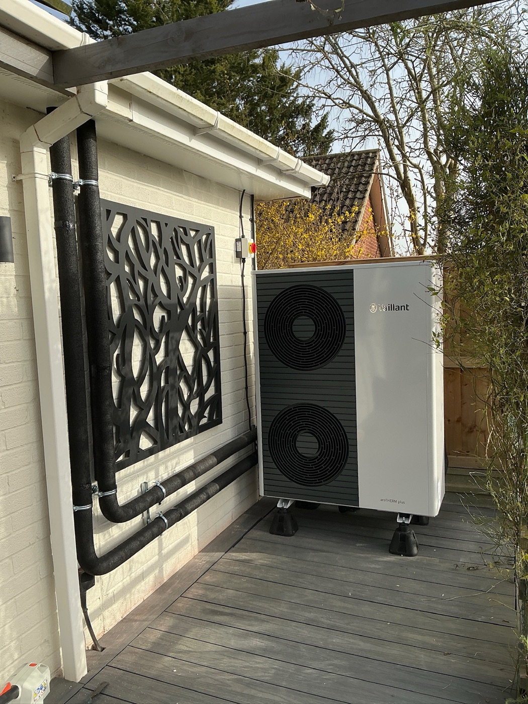 Air source heat pump installed on garden decking with insulated pipework