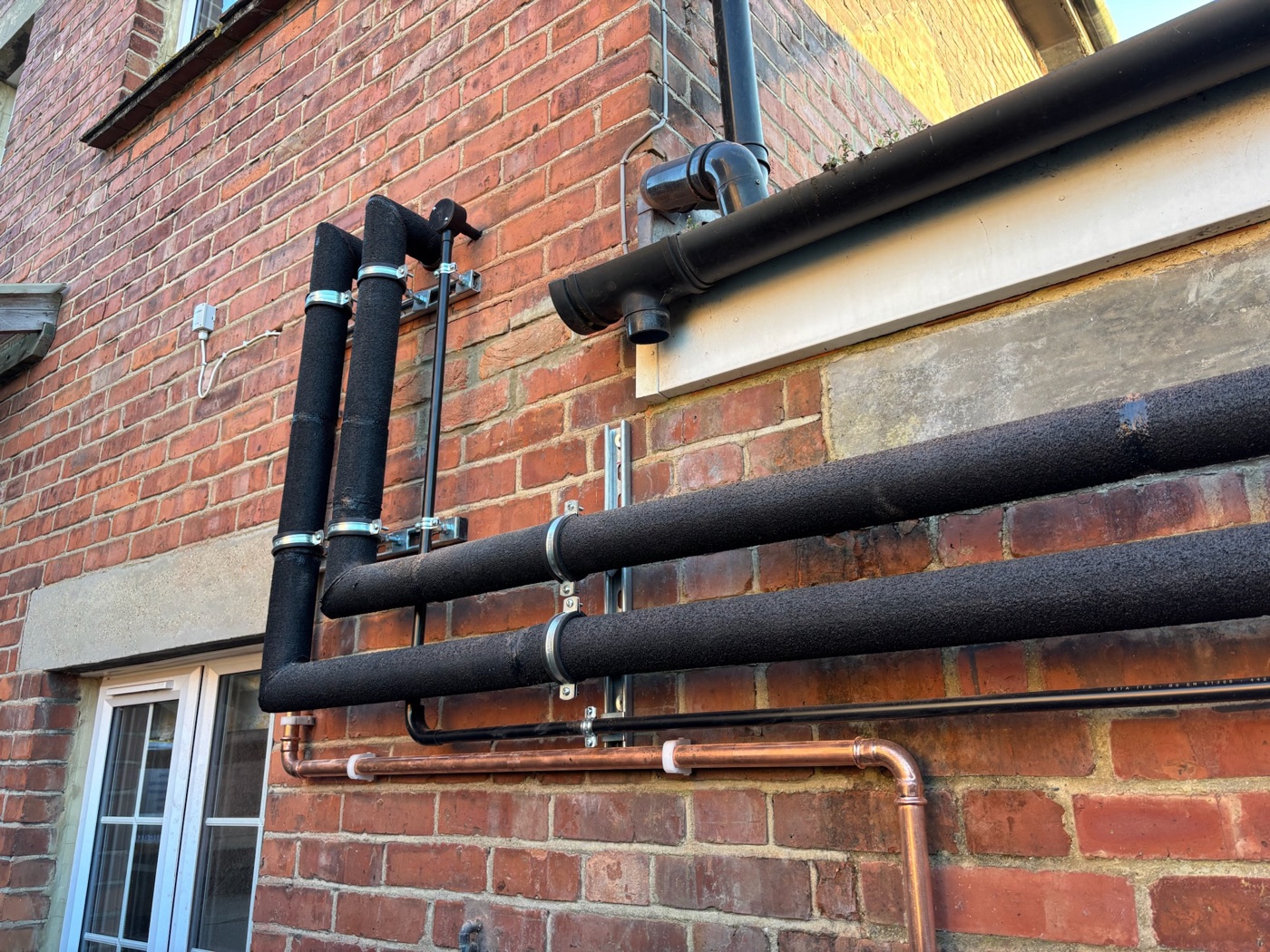 Neat insulated heat pump flow and return pipework along a brick wall