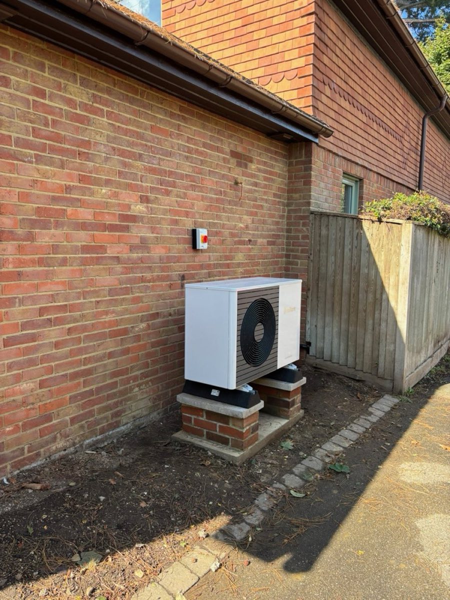 Air source heat pump fitted to a rear wall on brick plinths